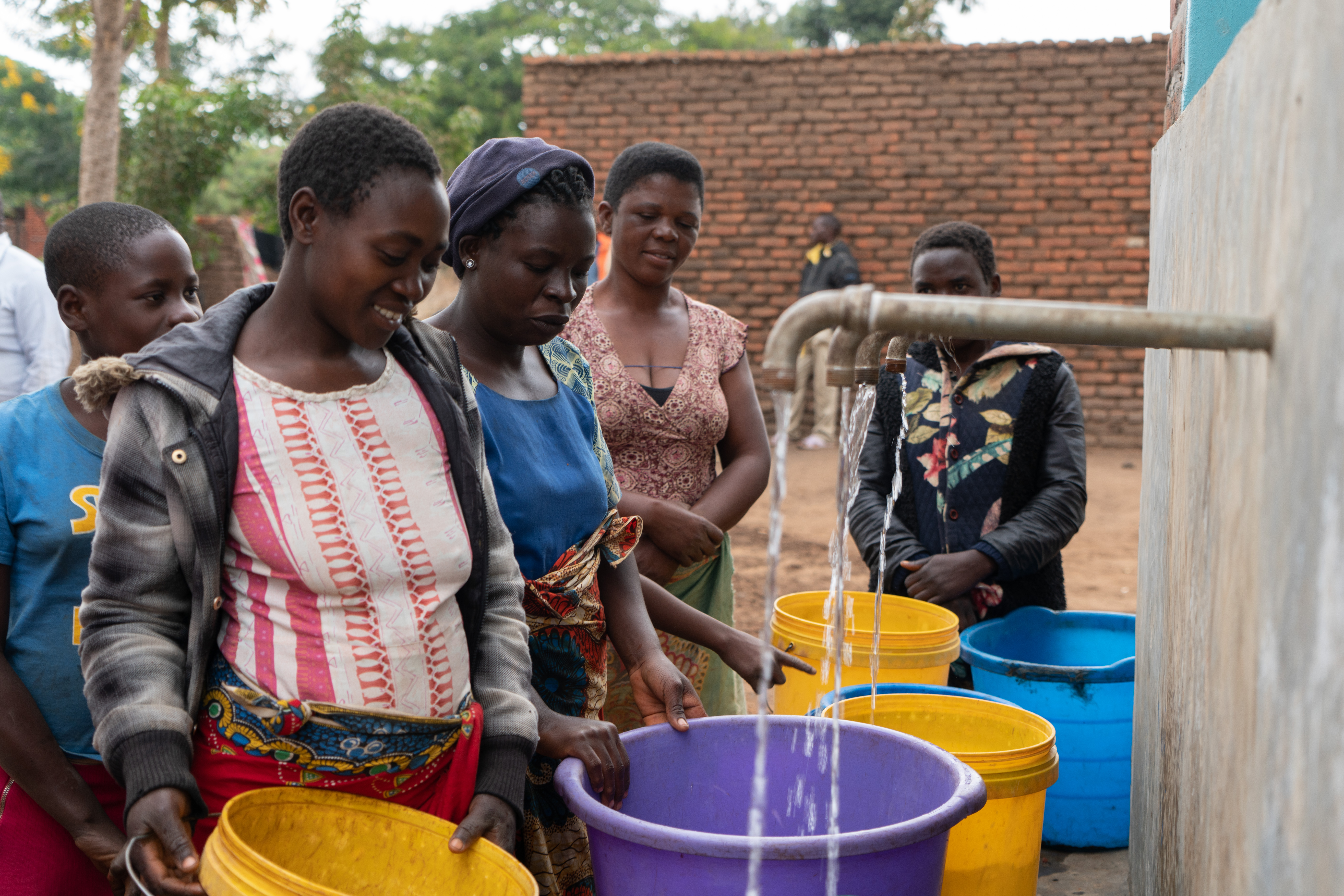 Women smiling as clean water runs from the taps of the new water kiosk in Chiswe village