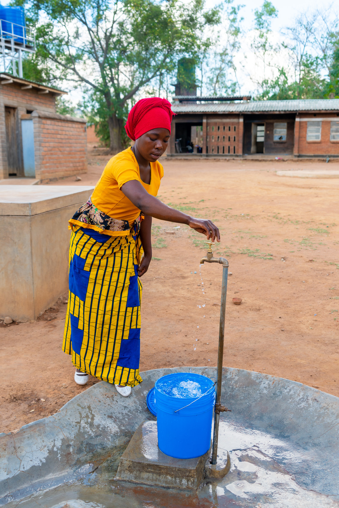Marriam Kadangwa, filling a bucket with water from a tap installed through the Deliver Life 2 Project